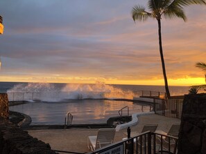 A pool with a view of the ocean at sunset, surrounded by stone walls and metal railings. - Garden Floor Unit, Ocean Front Condo Complex, Casa De Emdeko (Kailua-Kona)