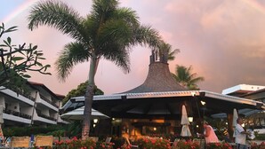 Ein Resort mit überdachter Außenbereich, Palmen und einem Gebäude mit einem markanten Kegeldach.