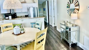 A modern kitchen with white cabinets, a stainless steel refrigerator, and a dining area with a round table and chairs.