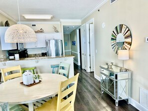 A modern kitchen with white cabinets, a stainless steel refrigerator, and a dining area with a round table and chairs.