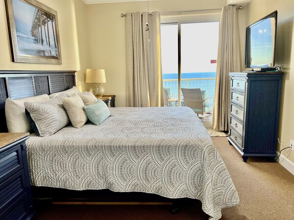 Un dormitorio con cama, cómoda, televisor, un cuadro y vista al océano.