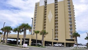 A high-rise hotel with a beige facade, multiple balconies, and a parking garage below.