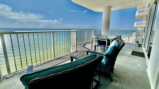 A balcony with a view of the ocean, a table with chairs, and a railing.
