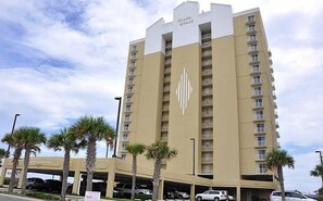 Un hotel moderno de gran altura con fachada color beige, varios balcones y un aparcamiento en la planta baja.