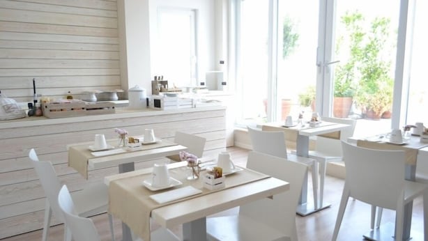 A bright, modern dining area with white furniture and large windows offering a view of the outdoors. - Gatto Bianco Le Terrazze (Bari)