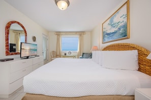 A bedroom with a large bed, a television, a desk, and a window with curtains.