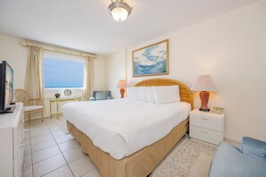 A bedroom with a bed, bedside lamps, a nightstand, a chair, a desk, a television, and a window with a view.