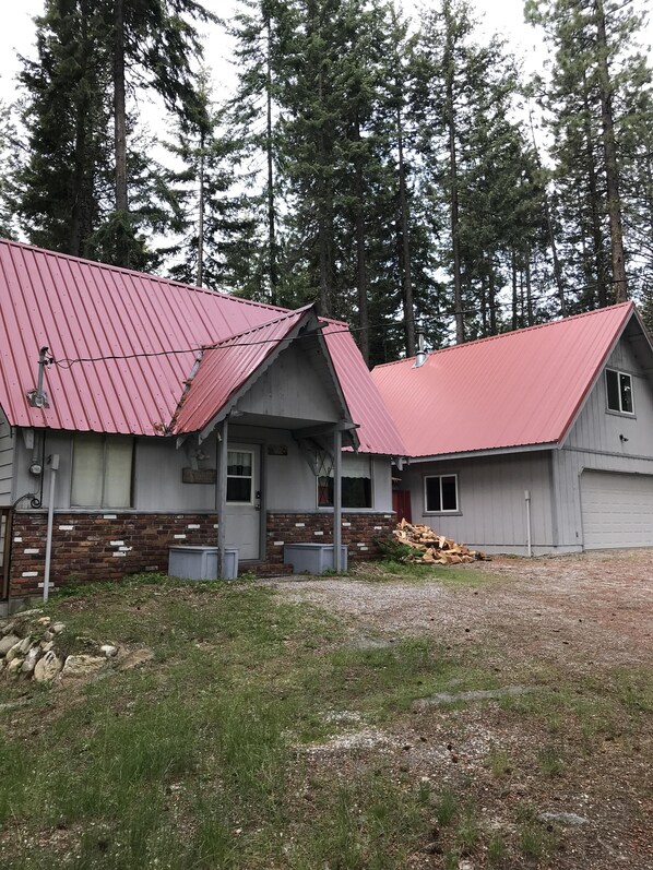 A building with a red roof, a brick lower section, and a small porch. There is a pile of firewood in front of the building. - Real Mountain Cabin with access to Fish Lake (Leavenworth)