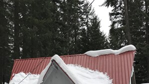A cabin with a red roof and white walls, surrounded by snow and trees.