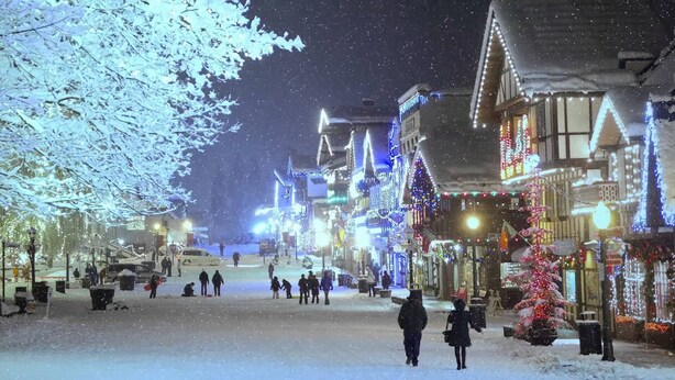 A snowy street with buildings adorned with lights, suggesting a festive atmosphere.