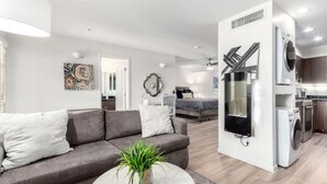 En modern lägenhet med en grå soffa, ett runt soffbord, en tvättmaskin och ett köksutrymme.