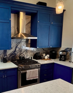 Eine Küche mit blauen Schränken, einem Gasherd, einem Backofen, einer Edelstahl-Dunstabzugshaube und einer Kaffeemaschine.