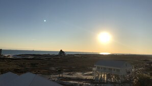 A coastal landscape with a house on stilts, a pier, and a clear sky.