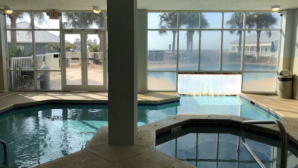 An indoor swimming pool with clear glass walls, a view of the beach, and an exit sign.