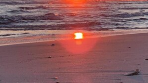 A beach at sunset with waves and a clear sky.