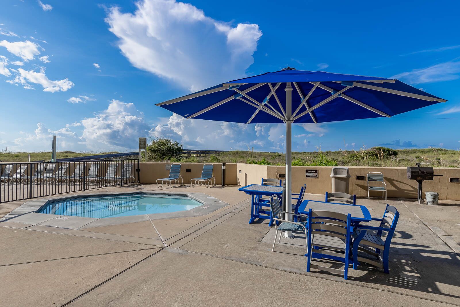 A pool area with a blue umbrella, lounge chairs, and a view of the landscape.