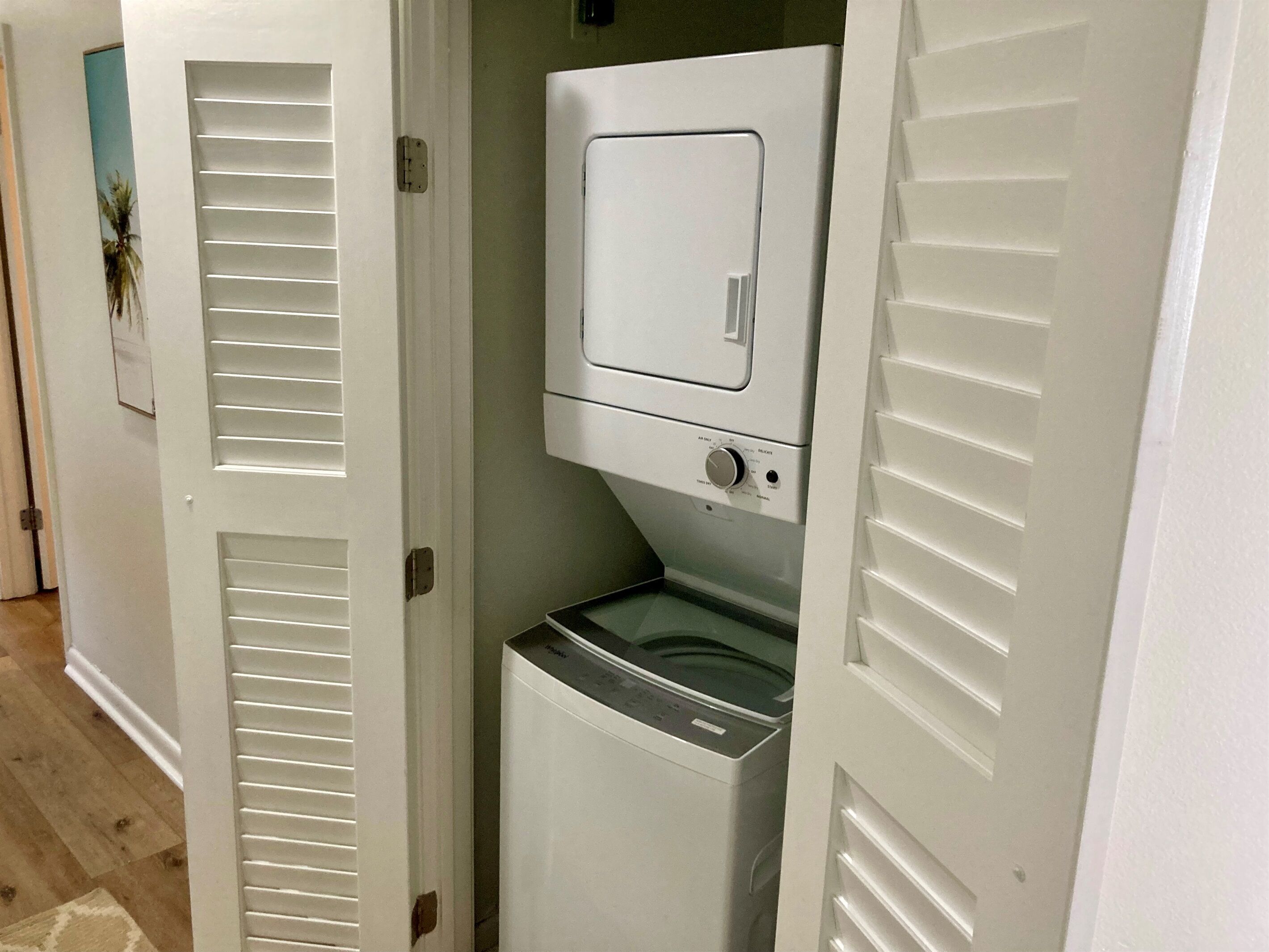 A laundry room with a front-loading washer and dryer, a door with a window, and a wooden floor.