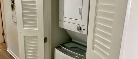 A laundry room with a front-loading washer and dryer, a door with a window, and a wooden floor.