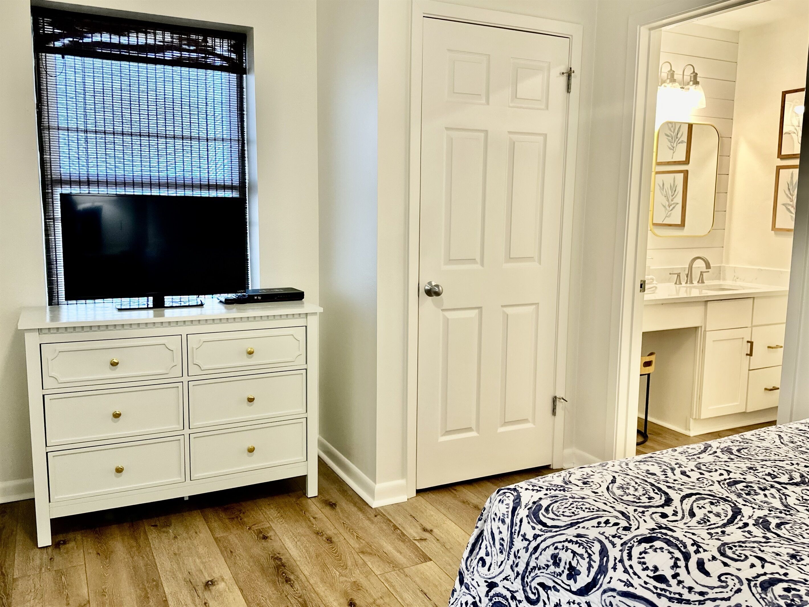 A bedroom with a bed, a dresser with drawers, a door, and a window with blinds.