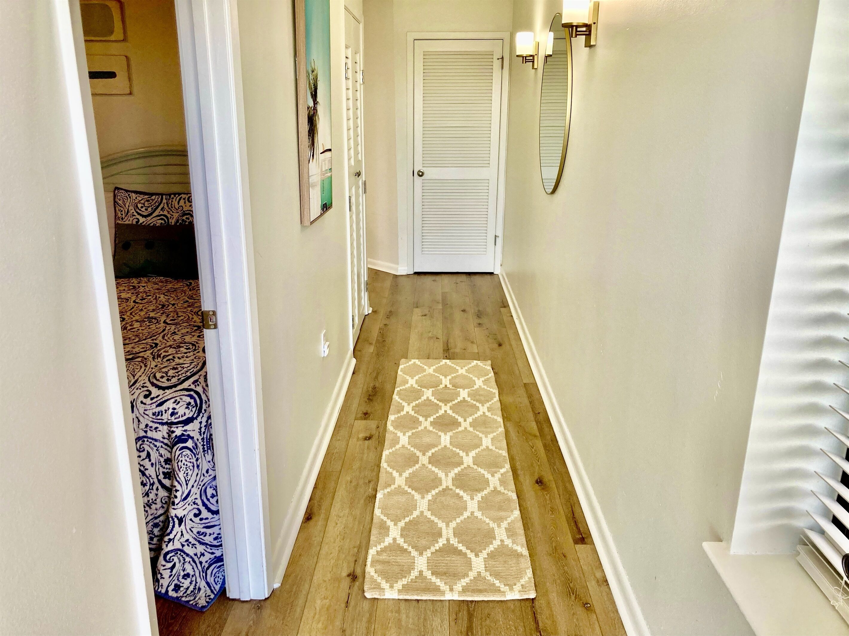 A narrow hallway with a patterned rug, a door, and a wall-mounted mirror.