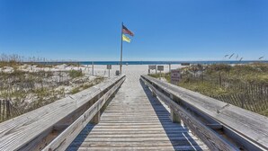 Une promenade en bois mène à une plage, et un panneau d’avertissement rappelle aux visiteurs de porter des chaussures de protection.