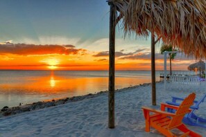 A beach scene with a sunset, wooden structures, and beach chairs.