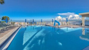 Ein klarer, blauer Swimmingpool mit Liegestühlen und Sonnenschirmen, umgeben von einem weißen Zaun und Palmen.