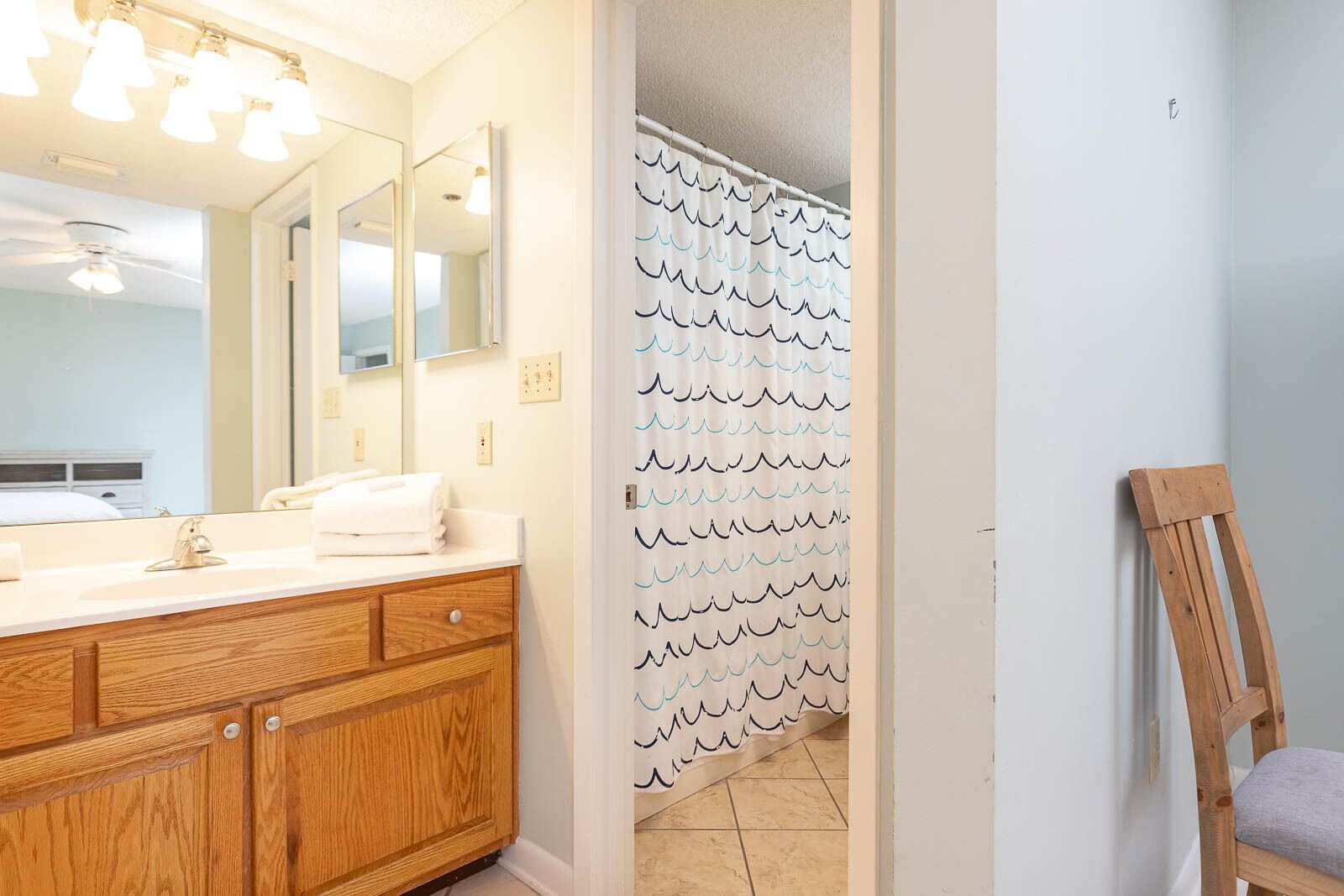 Une salle de bain avec un meuble-lavabo en bois, un grand miroir et une douche dotée d’un rideau à motifs ondulés.