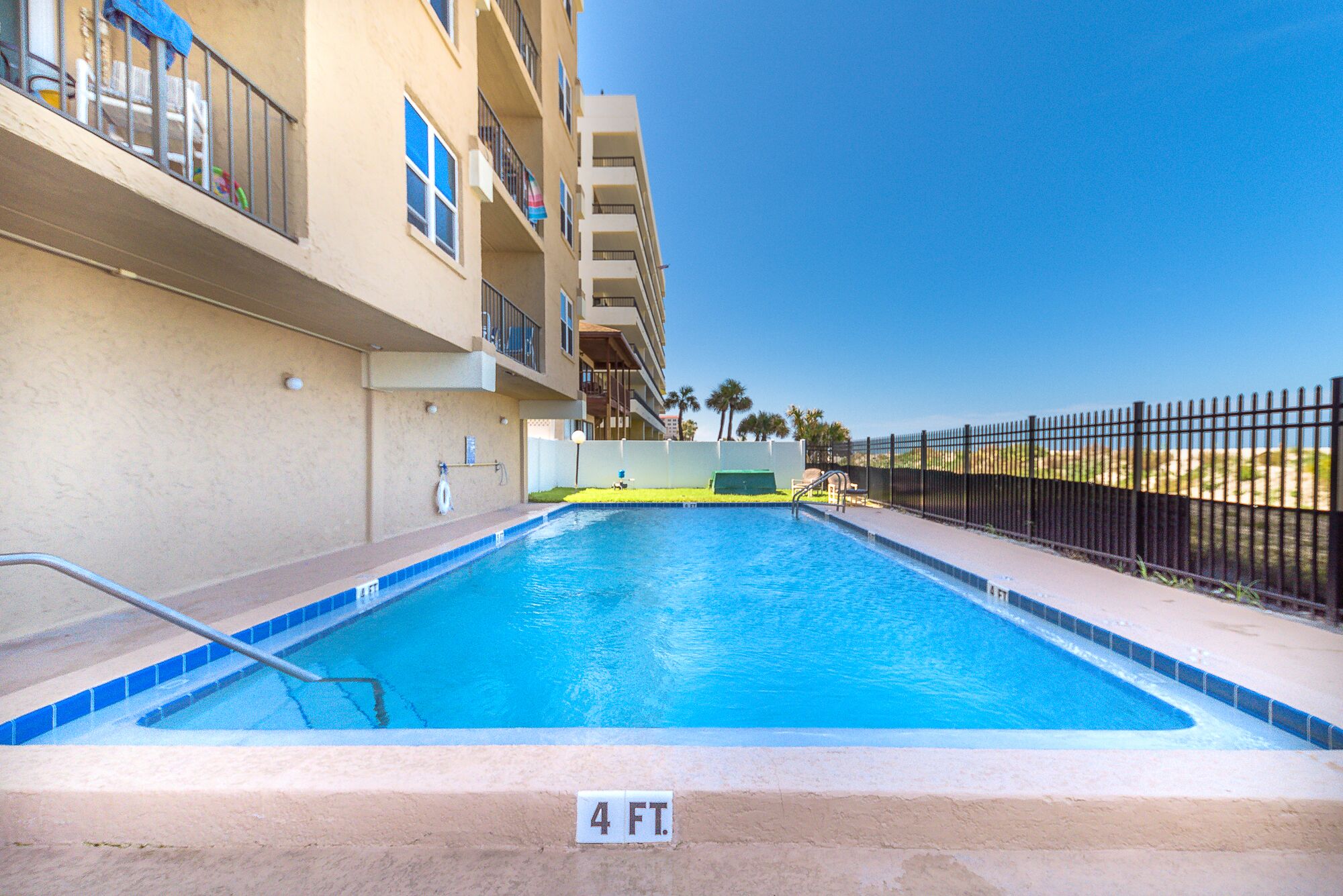 A swimming pool with a 4 FT depth marker, surrounded by a fence, with a building in the background.