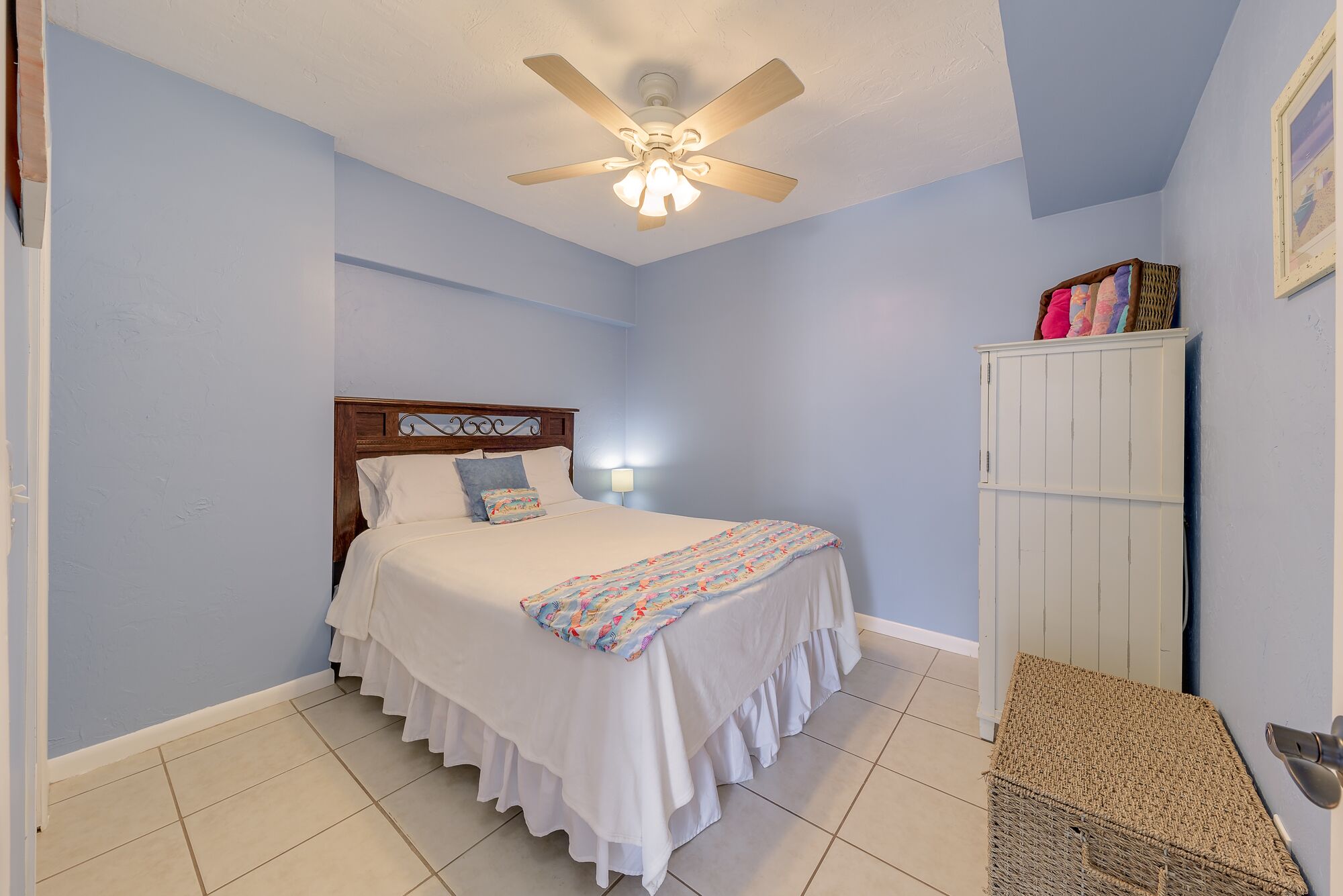 A bedroom with a bed, a ceiling fan, a nightstand, a wardrobe, and a wall-mounted lamp.