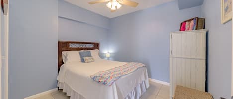 A bedroom with a bed, a ceiling fan, a nightstand, a wardrobe, and a wall-mounted lamp.