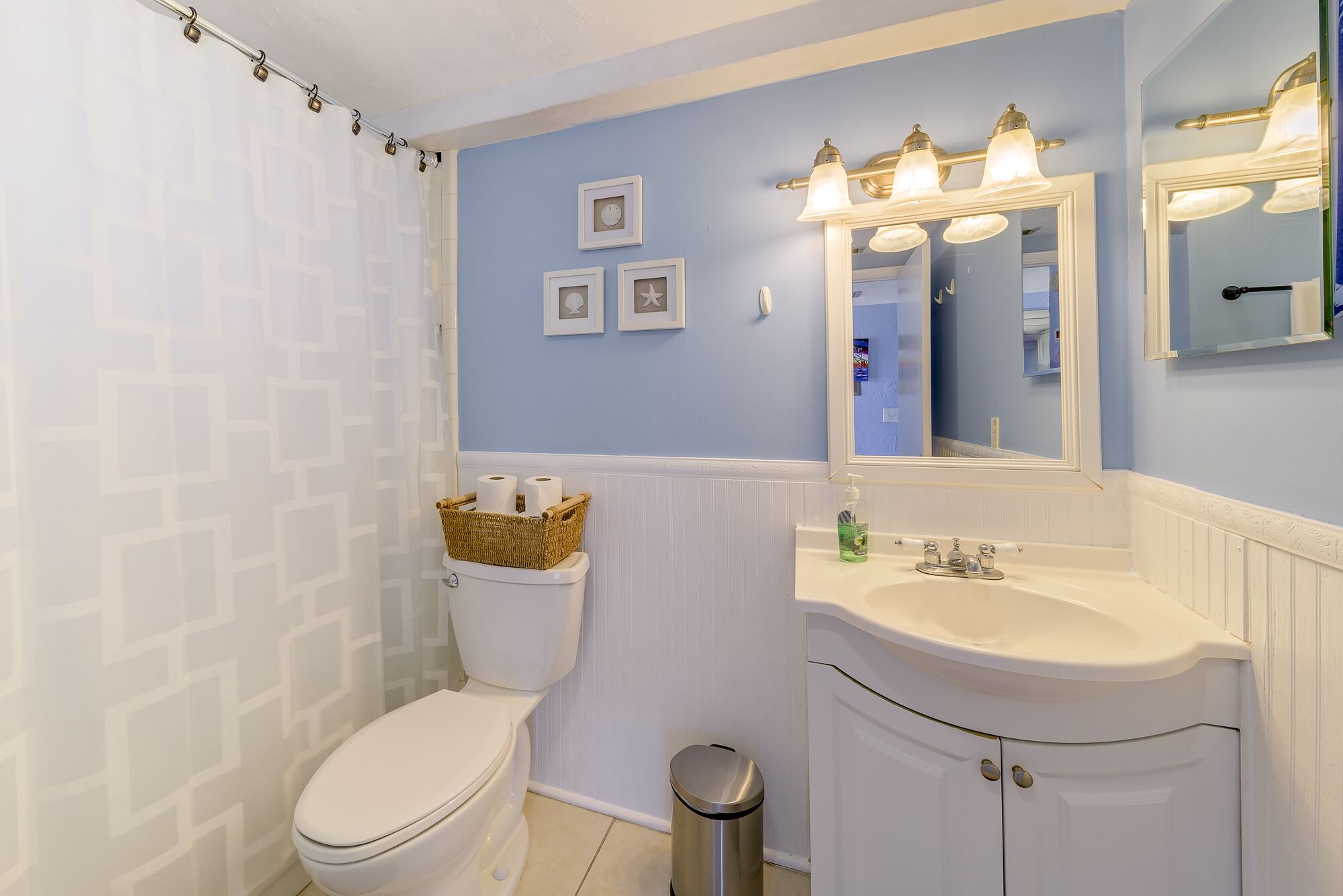 A bathroom with a toilet, a sink, a mirror, and a shower curtain.