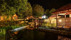 Escena nocturna serena con un estanque, un puente de piedra y edificios de madera con tejados rojos.