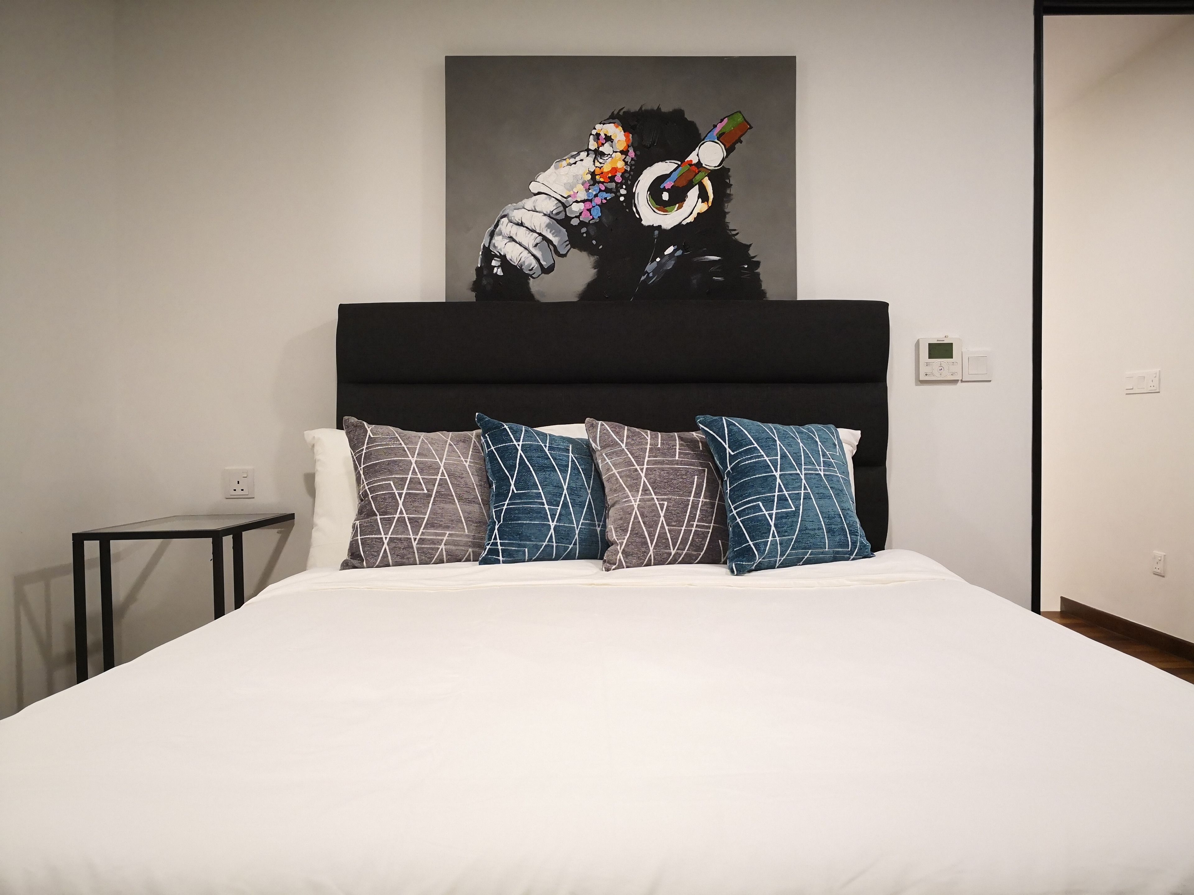 Una habitaci ón de hotel con una cama, cabecero y una obra de arte colgada en la pared.