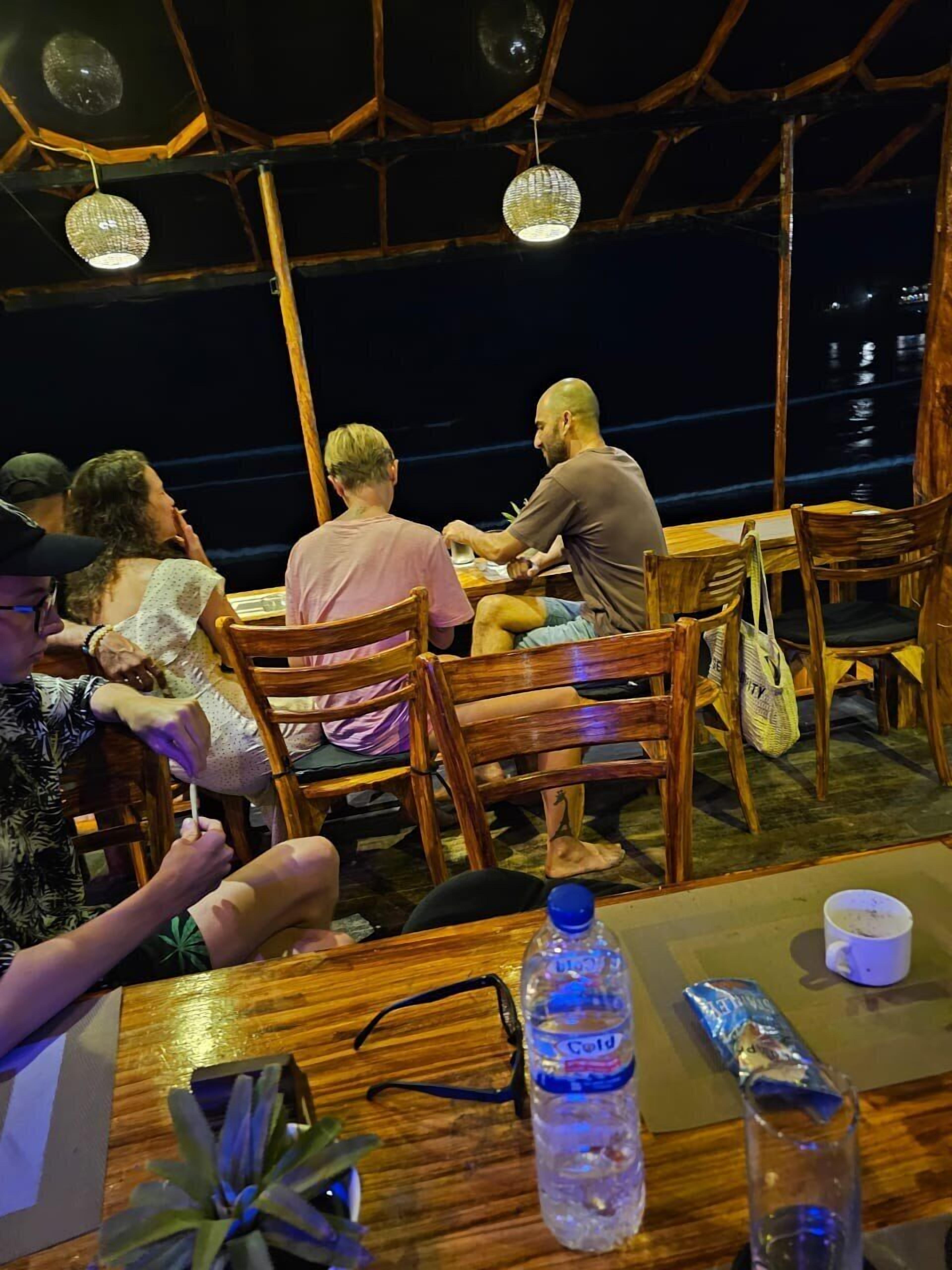 A wooden deck with tables and chairs, overlooking a body of water at night.