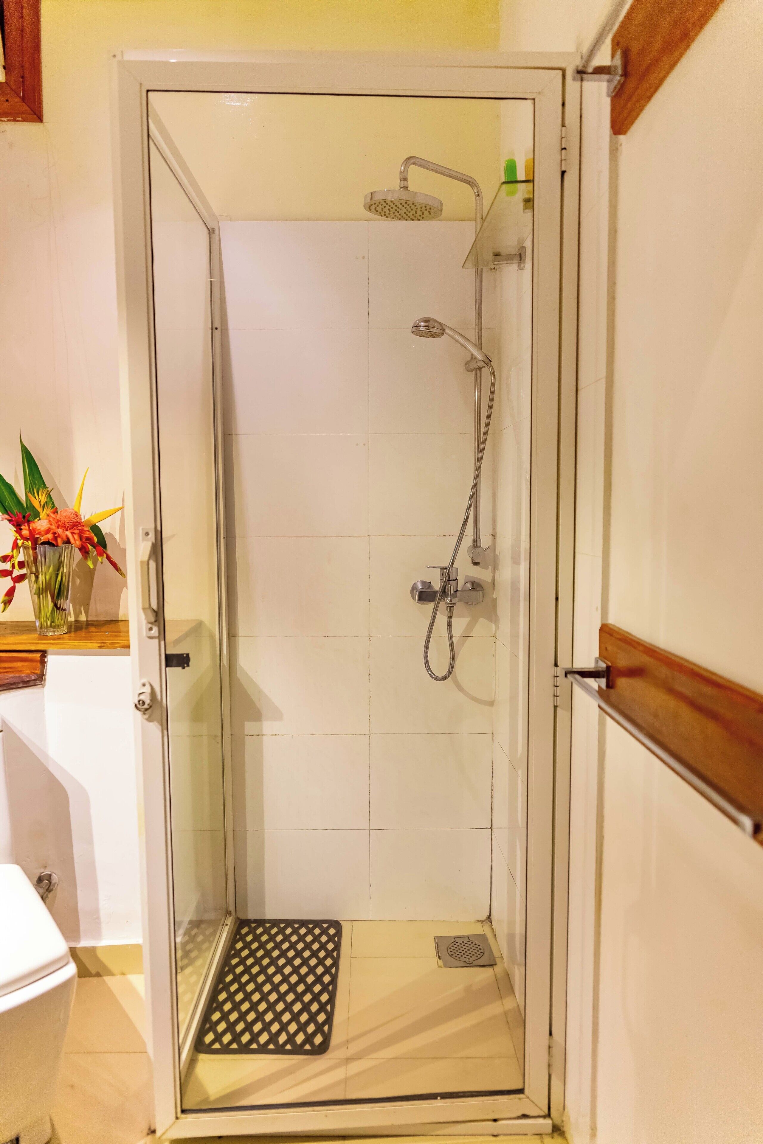 A glass-enclosed shower with a handheld showerhead, a handheld faucet, and a showerhead with a rain shower attachment.