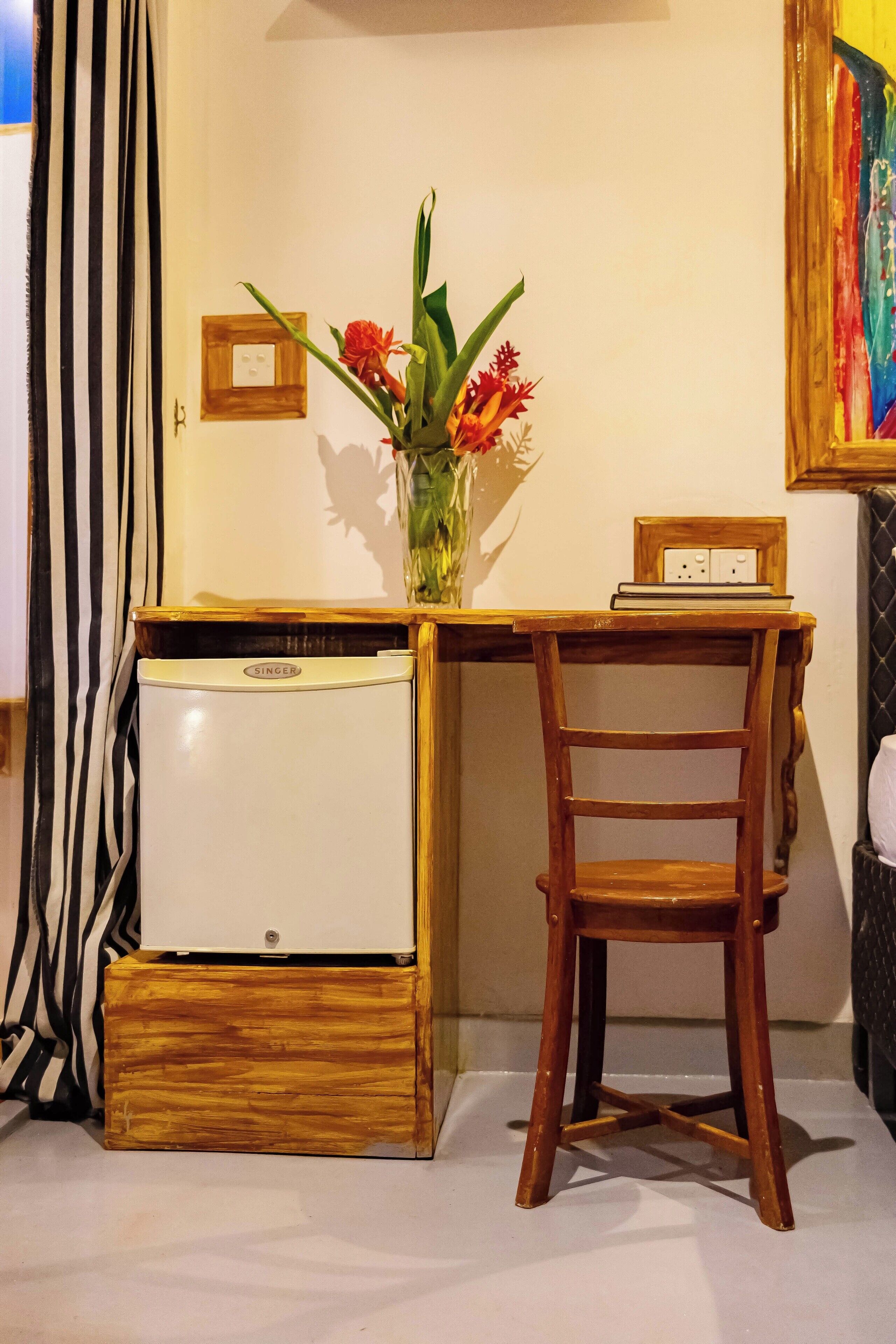 Una piccola cucina componibile con frigorifero bianco, una sedia di legno, un tavolino e un vaso con fiori.
