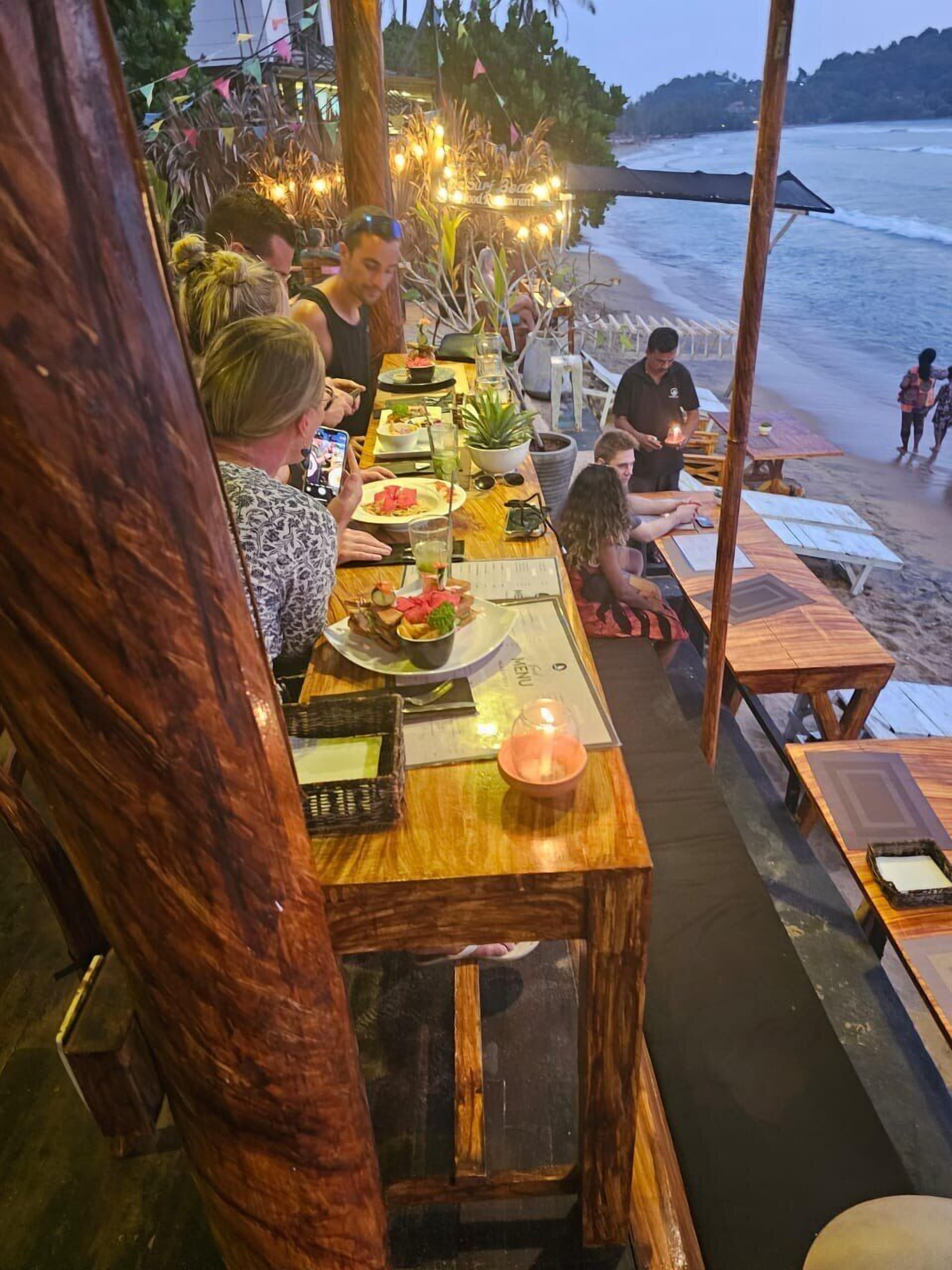 A beachfront restaurant with wooden tables and chairs, a menu, and a view of the ocean.
