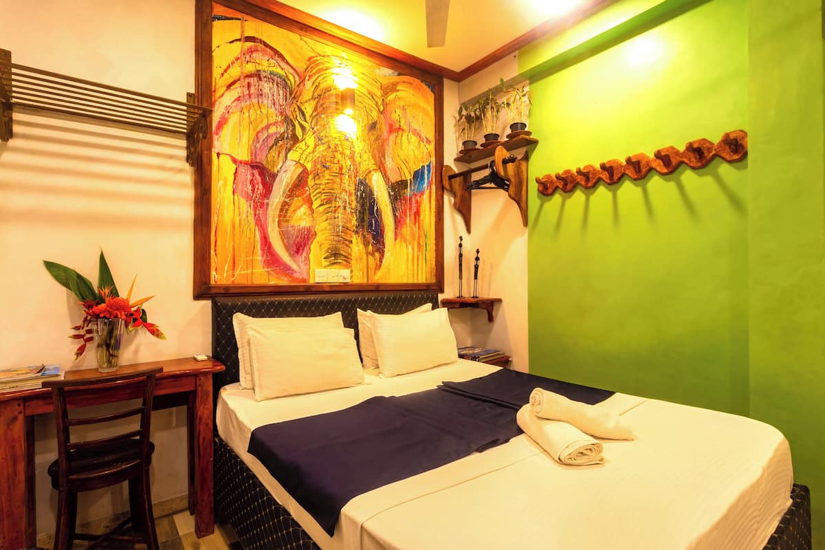 A hotel room with a bed, a desk with a chair, a painting on the wall, and a green accent wall.