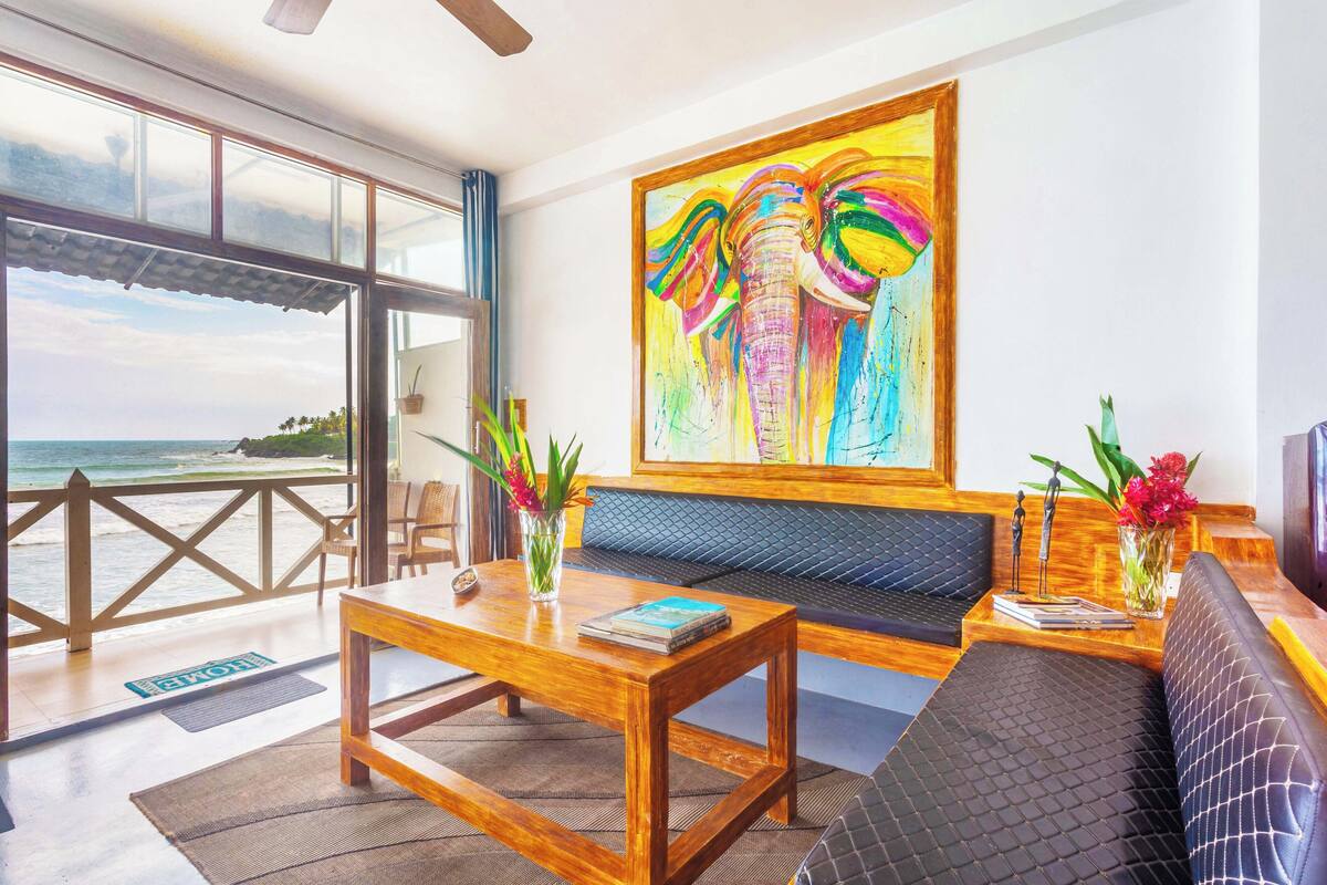 A modern living room with a wooden coffee table, a sofa, and a large painting of elephants.