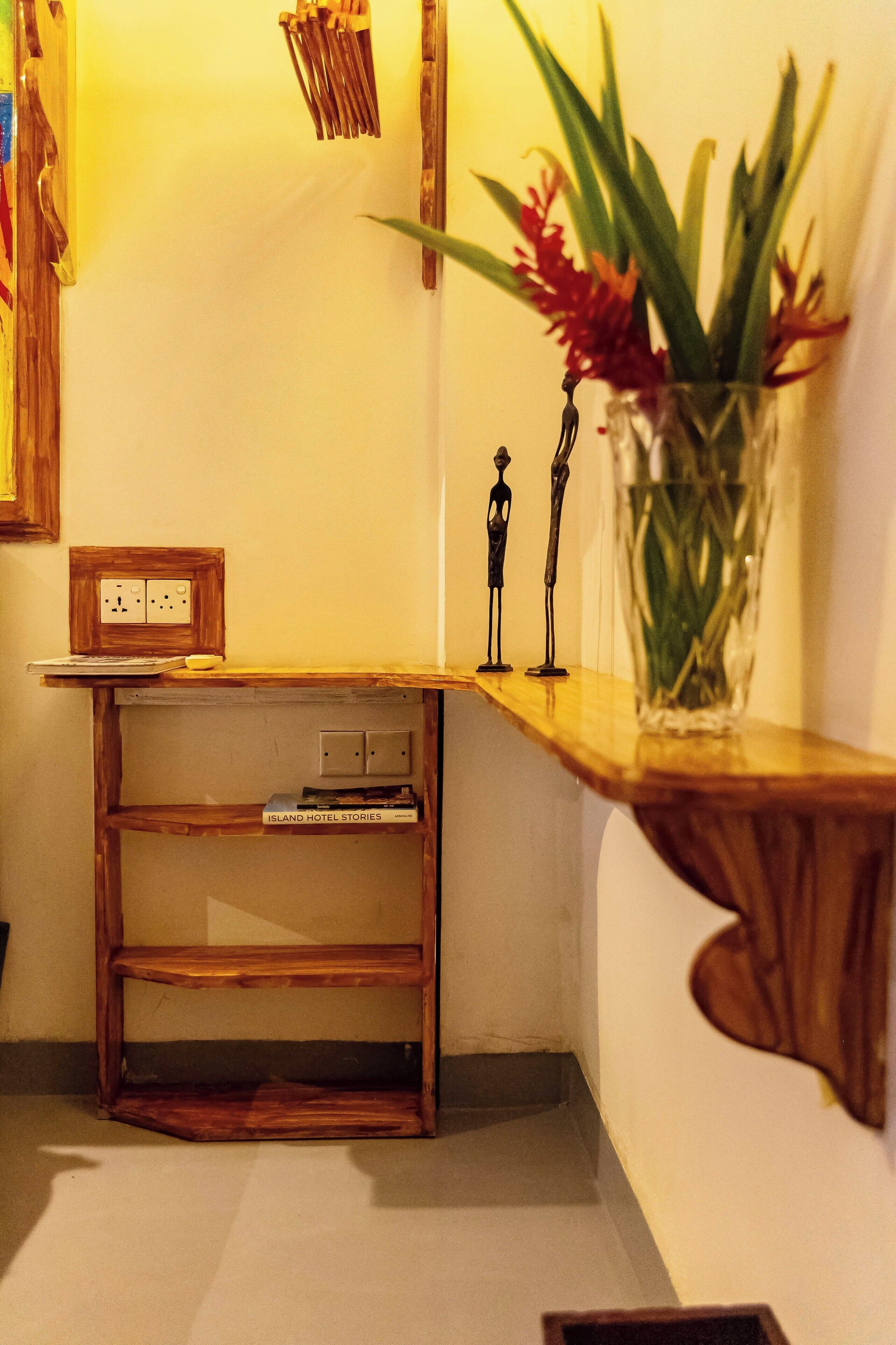 A corner of a room with a wooden shelf, a vase with flowers, and a small statue.