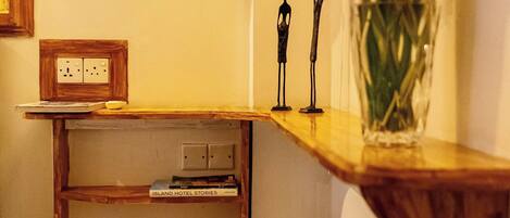 A corner of a room with a wooden shelf, a vase with flowers, and a small statue.