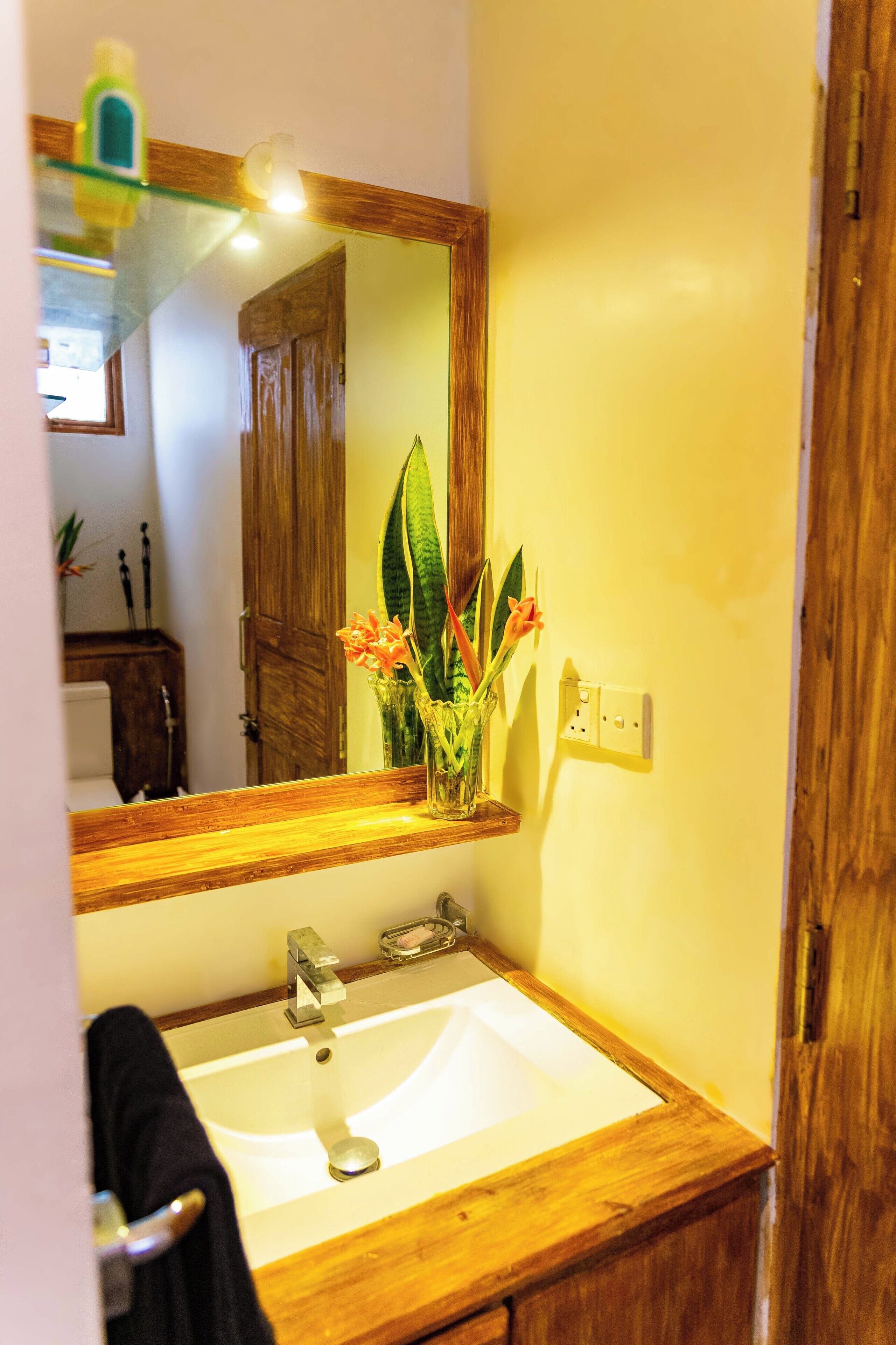 A bathroom with a wooden vanity, a sink, a mirror, and a vase with flowers.