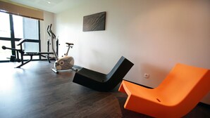 Een moderne kamer met een hometrainer, een zwarte en oranje stoel en een groot raam.
