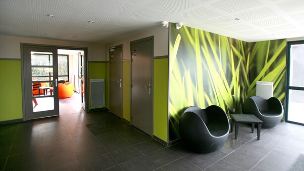 Een moderne wachtruimte met een groene muurschildering, zitplaatsen en een deur naar buiten.