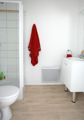 Une salle de bain avec des toilettes blanches, un lavabo blanc et une serviette rouge accrochée au mur.