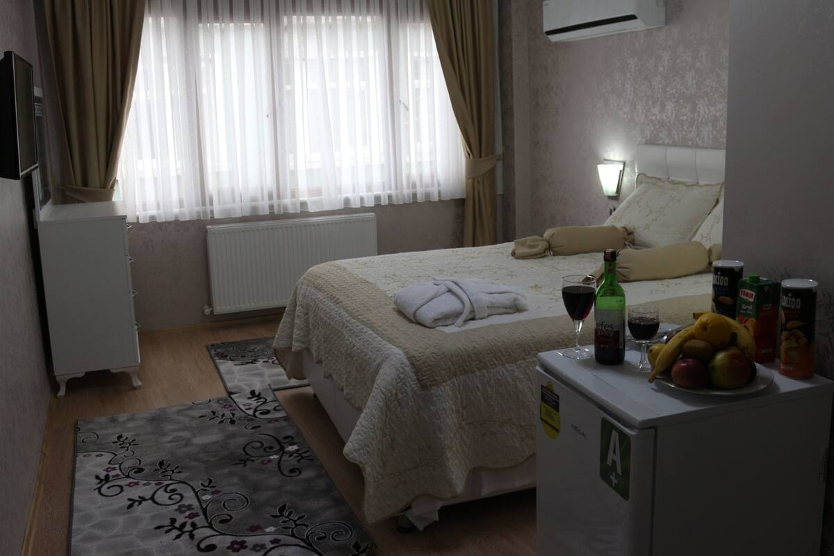 Une chambre d’hôtel avec un lit, un bureau doté d’un réfrigérateur, une bouteille de vin et des fruits posés sur le bureau.