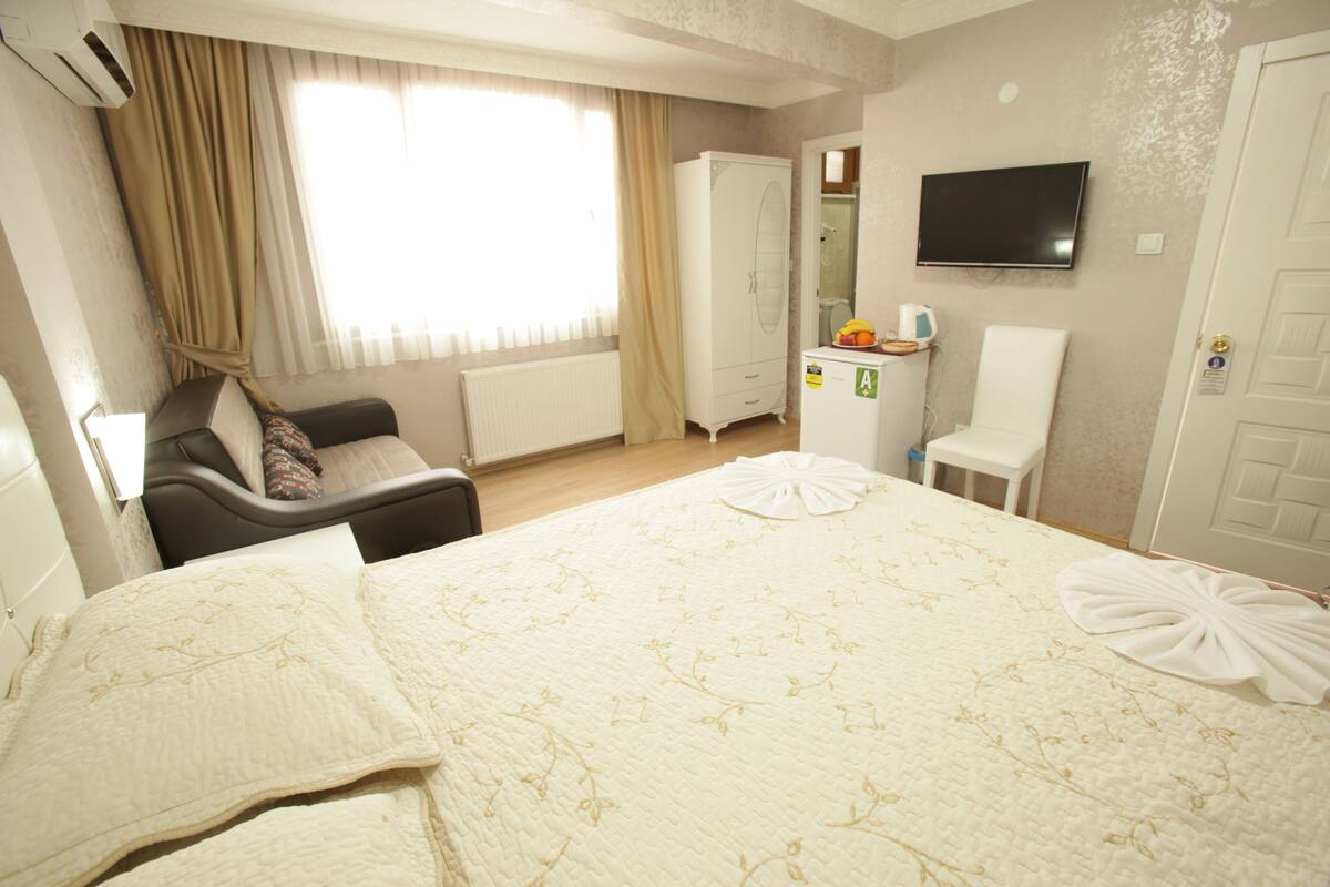 Une chambre d’hôtel comprenant un lit, une armoire, un bureau avec une chaise, une télévision et une fenêtre avec des rideaux.