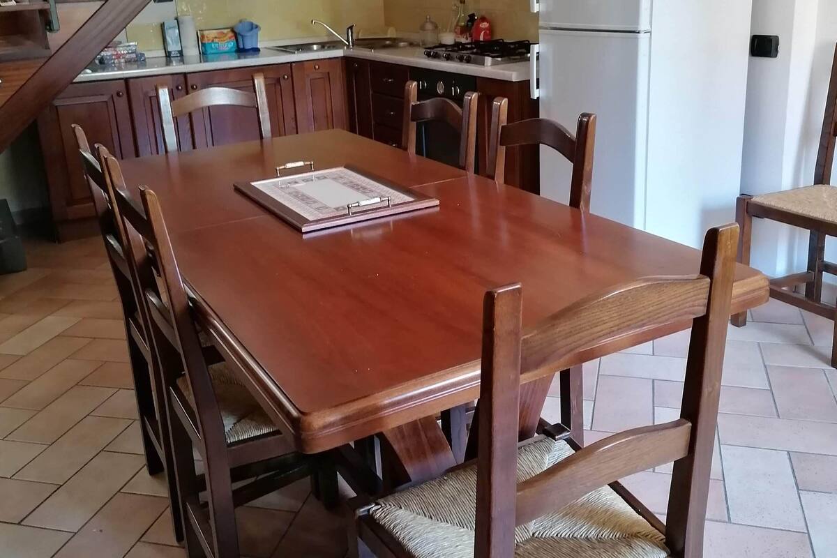 A spacious kitchen with a dining area, wooden cabinets, a built-in bookshelf, and a staircase.