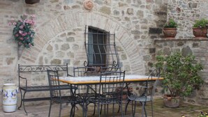 Un muro de piedra con una ventana, una mesa con sillas y plantas en macetas.